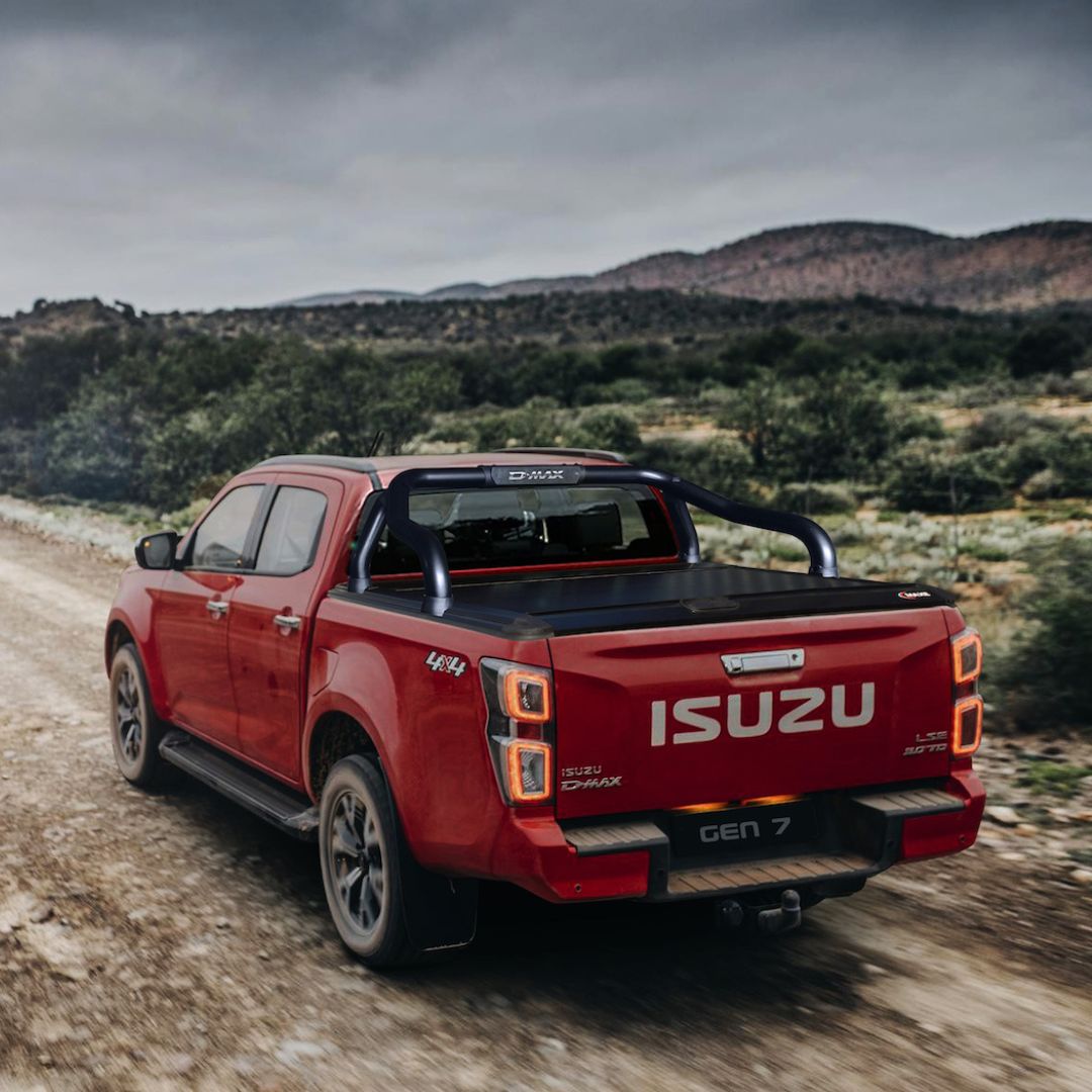Isuzu D-Max with Maxe RollaTop roller shutter and sports bar driving on a gravel road, showcasing premium load bin protection and OEM fit.